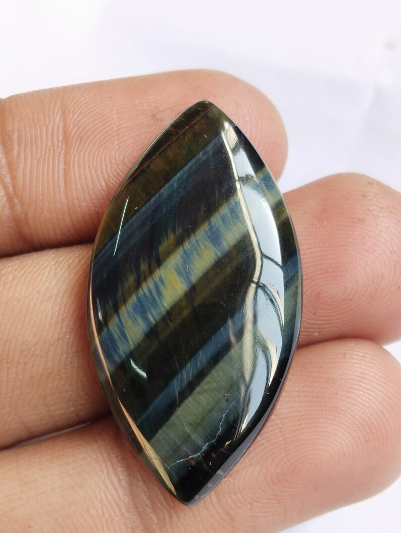 May include: A blue and gold tiger's eye cabochon gemstone with a teardrop shape. The gemstone has a smooth, polished surface and a unique, iridescent sheen.