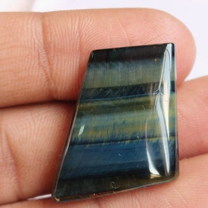 May include: A blue and gold tiger's eye gemstone cabochon with a faceted, irregular shape. The stone has a striated pattern and a glossy finish.