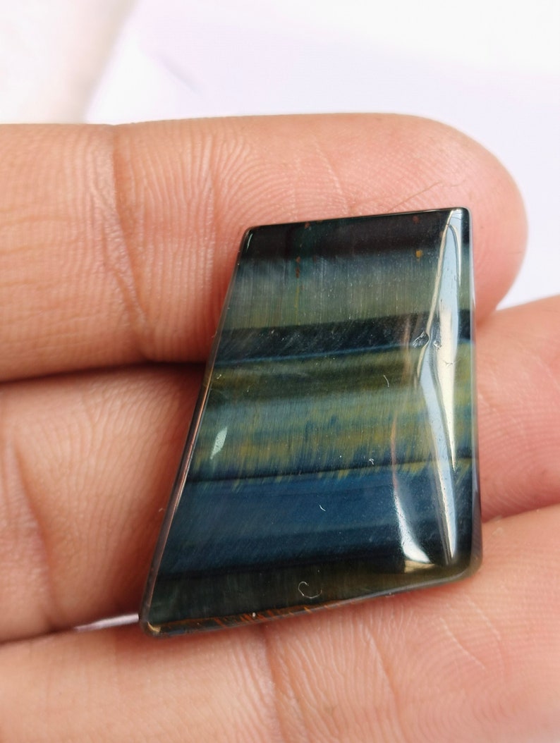 May include: A blue and gold tiger's eye gemstone cabochon with a faceted, irregular shape. The stone has a striated pattern and a glossy finish.