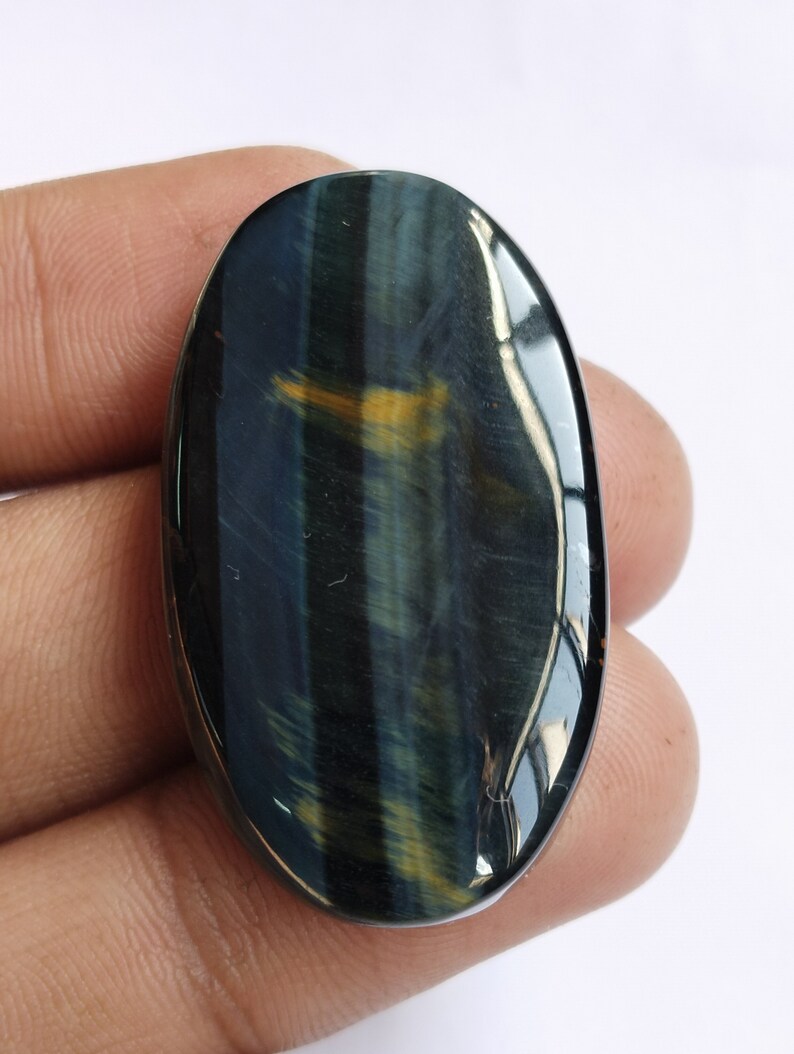 May include: A blue and gold tiger's eye cabochon, oval shaped, with a smooth, polished surface.
