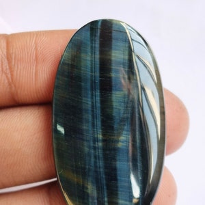 May include: A blue and gold tiger's eye cabochon gemstone, oval shaped, with a smooth, polished surface.