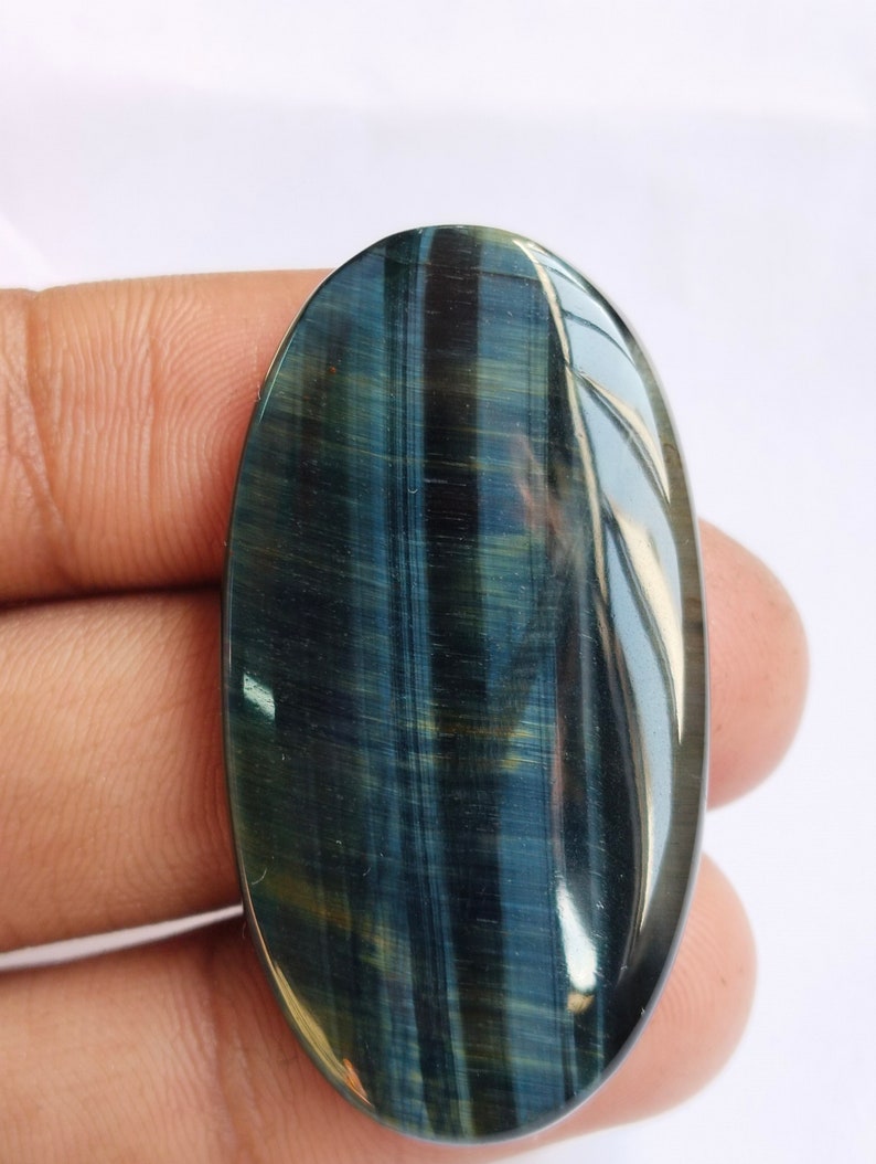May include: A blue and gold tiger's eye cabochon gemstone, oval shaped, with a smooth, polished surface.