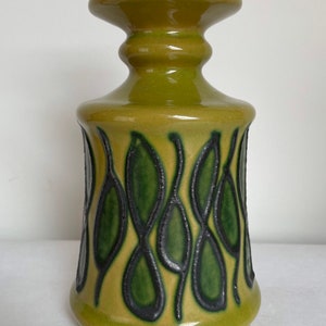 Könnte beinhalten: Eine grüne Keramikvase mit einem schwarzen und grünen Blattdesign. Die Vase hat einen breiten Boden und einen schmalen Hals.