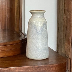 May include: A light blue ceramic vase with a white glaze and a subtle speckled pattern. The vase has a rounded body and a slightly flared opening.