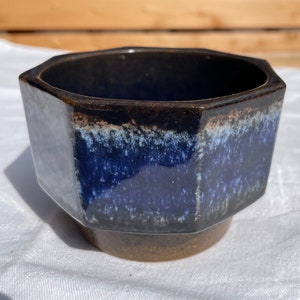 May include: Octagonal ceramic planter with a dark brown rim and a blue and white glaze. The planter has a mottled blue and white glaze with a dark brown base.