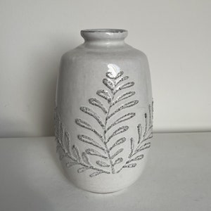 Peut inclure: Vase en céramique blanche avec un motif floral en relief. Le vase a un corps arrondi et un col étroit.