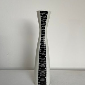 May include: A white ceramic vase with a black and white geometric pattern. The vase has a narrow neck and a wide base.
