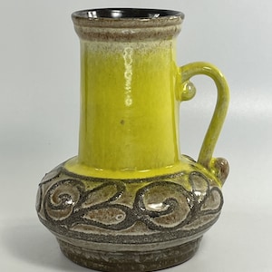 Peut inclure: Un vase en céramique jaune avec un glaçage brun et un motif en spirale. Le vase a une anse et une base large.