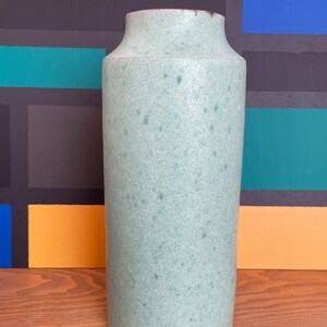 Könnte beinhalten: Eine hellgrüne Keramikvase mit gesprenkeltem Finish. Die Vase hat eine zylindrische Form und einen abgerundeten Boden.