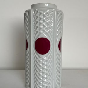 May include: White ceramic vase with a geometric design and two large, red circles.