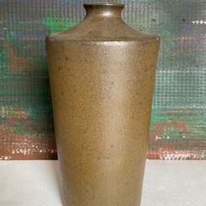 Könnte beinhalten: Eine hohe, braune Keramikvase mit gesprenkeltem Überzug. Die Vase hat einen abgerundeten Boden und einen schmalen Hals.