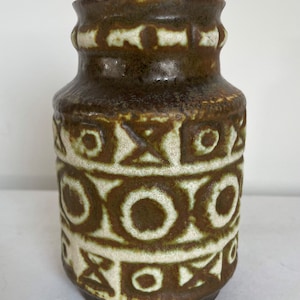 May include: A brown ceramic vase with a textured surface and geometric patterns in white and brown. The vase has a cylindrical shape with a slightly flared top and a base. The vase is approximately 7 inches tall.
