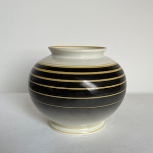 May include: A white ceramic vase with black and gold stripes. The vase has a round body and a small base.