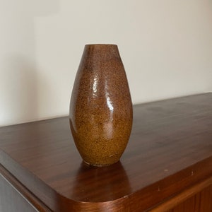 May include: A teardrop-shaped ceramic vase with a glossy, speckled brown glaze. The vase features a narrow opening at the top and a wider, rounded body that tapers towards the base, showcasing a consistent earthy tone throughout the entire surface.