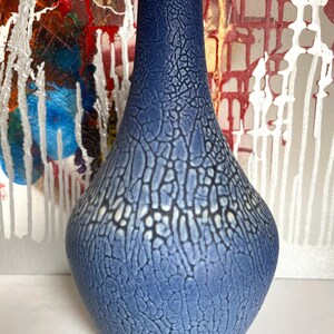 May include: A blue ceramic vase with a textured, crackled surface. The vase has a bulbous base that tapers to a narrow neck. The colour transitions from a darker blue at the top to a lighter blue towards the base. Decorative home decor.