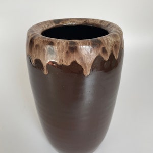 Könnte beinhalten: Eine hohe, dunkelbraune Keramikvase mit einer breiten Öffnung. Der Rand weist einen tropfenden Glaseffekt in Beige- und Brauntönen auf. Die Vase hat eine glatte, glänzende Oberfläche und eine zylindrische Form, geeignet für Blumen oder als dekoratives Element.