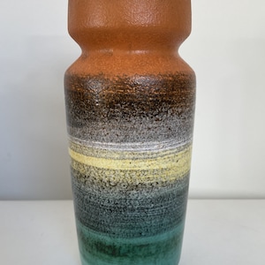 May include: A ceramic vase with a brown, black, white, and green glaze. The vase has a wide mouth and a narrow base.