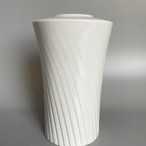 Könnte beinhalten: Weiße Keramikvase mit einem wirbelnden, strukturierten Design. Die Vase ist hoch und schlank, mit einer breiten Öffnung an der Oberseite.