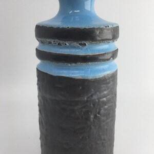 May include: A blue and black ceramic vase with a textured black base and three bands of black glaze around the middle. The vase has a narrow neck and a slightly flared lip.