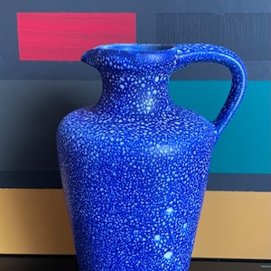 May include: A blue ceramic pitcher with a speckled white glaze. The pitcher has a wide mouth and a handle.