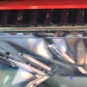 Op de afbeelding: Een rode plastic ventilatiekap voor een oven. De ventilatiekap heeft een reeks kleine gaten om luchtcirculatie mogelijk te maken.