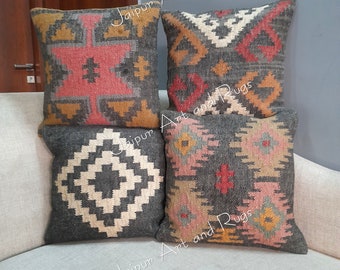 May include: Four decorative throw pillows with geometric patterns in shades of gray, pink, brown, and white. The pillows are arranged in a stack on a light gray couch.