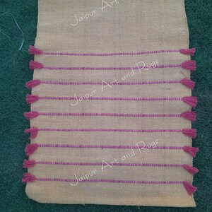 May include: A yellow and pink striped rug with tassels on the ends. The rug has the text "Jaipur Art and Rugs" printed on it.