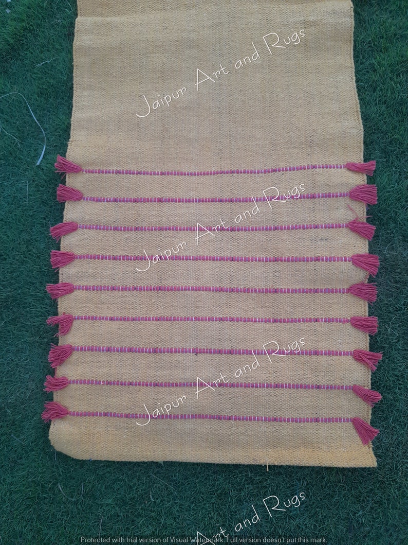 May include: A yellow and pink striped rug with tassels on the ends. The rug has the text "Jaipur Art and Rugs" printed on it.