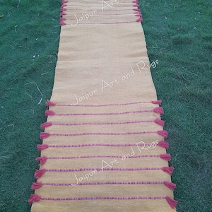 May include: A yellow and pink striped runner rug with pink tassels on each end. The rug has the text "Jaipur Art and Rugs" printed on it.