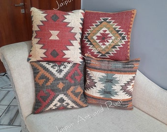 May include: Four decorative throw pillows with geometric patterns in shades of red, brown, beige, and blue. The pillows are arranged on a white couch.