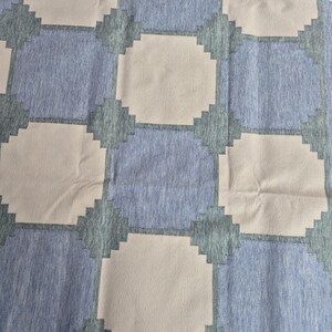 May include: A textile featuring a repeating geometric pattern of light beige octagons alternating with blue squares. The blue squares have a heathered texture, while the beige octagons are solid. Dark teal stepped edges connect the shapes.