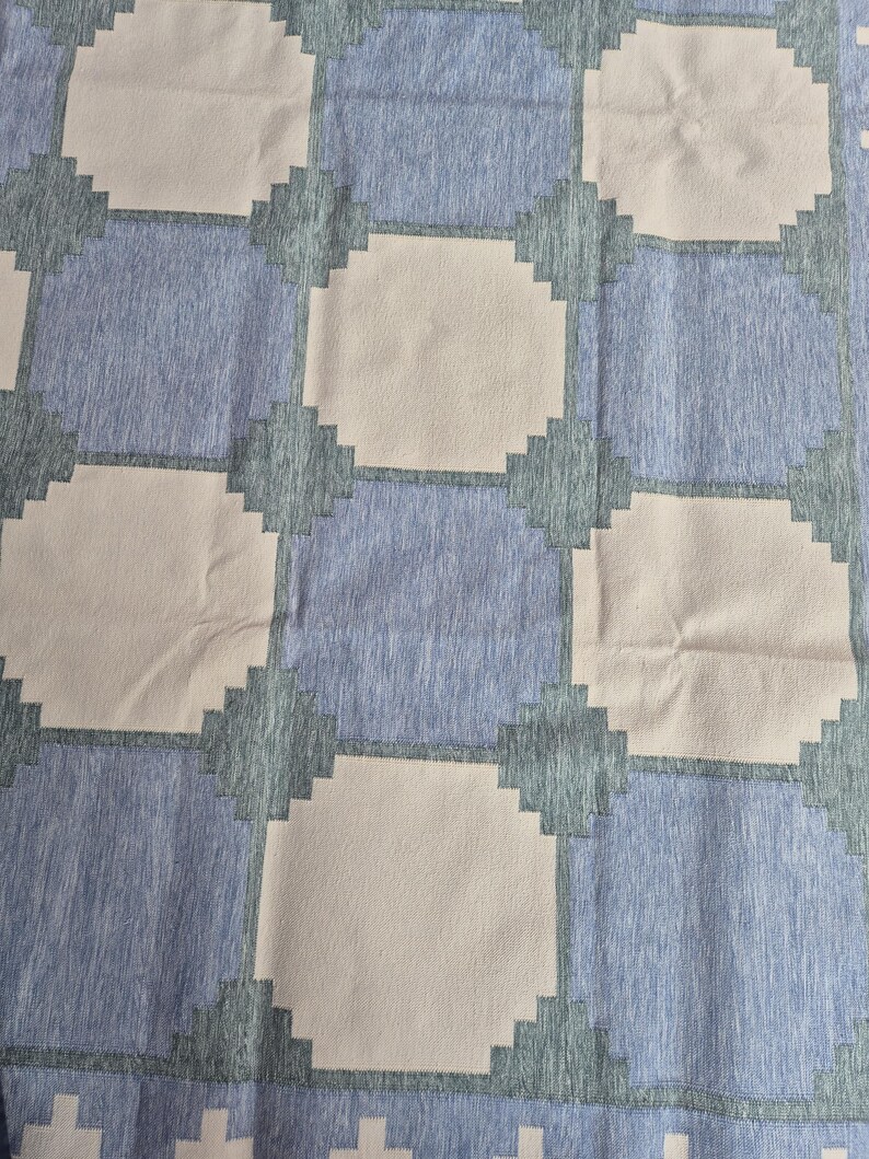 May include: A textile featuring a repeating geometric pattern of light beige octagons alternating with blue squares. The blue squares have a heathered texture, while the beige octagons are solid. Dark teal stepped edges connect the shapes.