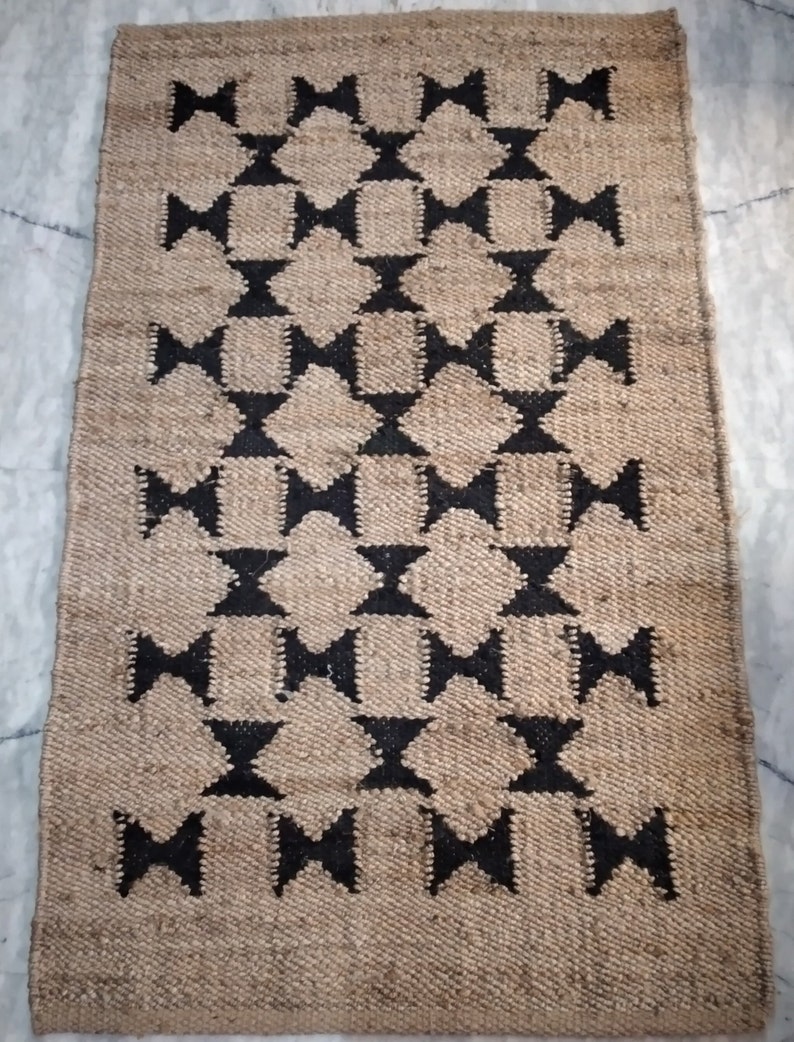May include: A brown and black jute rug with a geometric pattern. The rug has a diamond shape with a black bow tie in the center of each diamond.