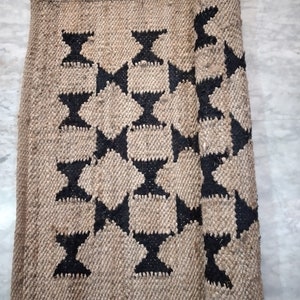 May include: A brown and black woven rug with a geometric pattern. The rug is rolled up on one side.