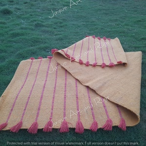 May include: Two yellow and pink striped rugs with tassels on a green grassy surface. The rugs are folded in half and the tassels are visible on both sides.