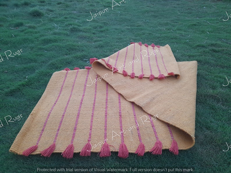 May include: Two yellow and pink striped rugs with tassels on a green grassy surface. The rugs are folded in half and the tassels are visible on both sides.