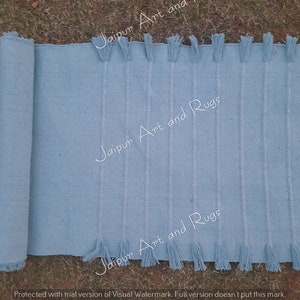 May include: A light blue woven rug with fringe on both ends. The rug is rolled up on the left side of the image.
