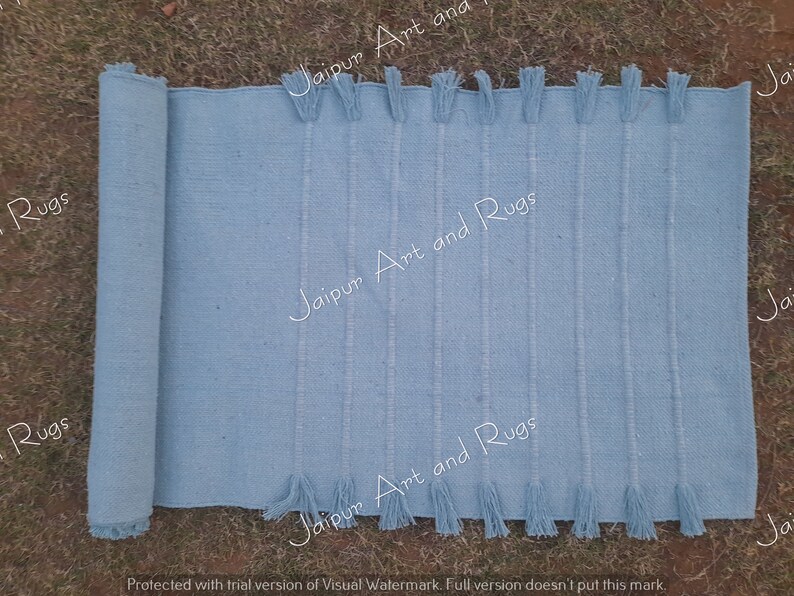May include: A light blue woven rug with fringe on both ends. The rug is rolled up on the left side of the image.