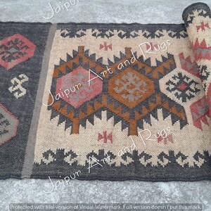May include: A handwoven rug with a geometric pattern in shades of brown, beige, and red. The rug has a fringe on the ends and is rolled up.