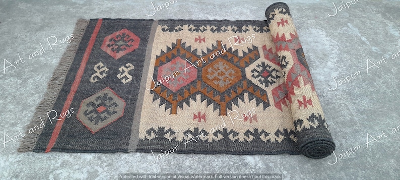 May include: A handwoven rug with a geometric pattern in shades of brown, beige, and red. The rug has a fringe on the ends and is rolled up.