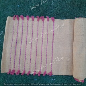 May include: A light beige runner rug with pink stripes and tassels. The rug is rolled up on the right side of the image. The text "Jaipur Art and Rugs" is visible on the rug.