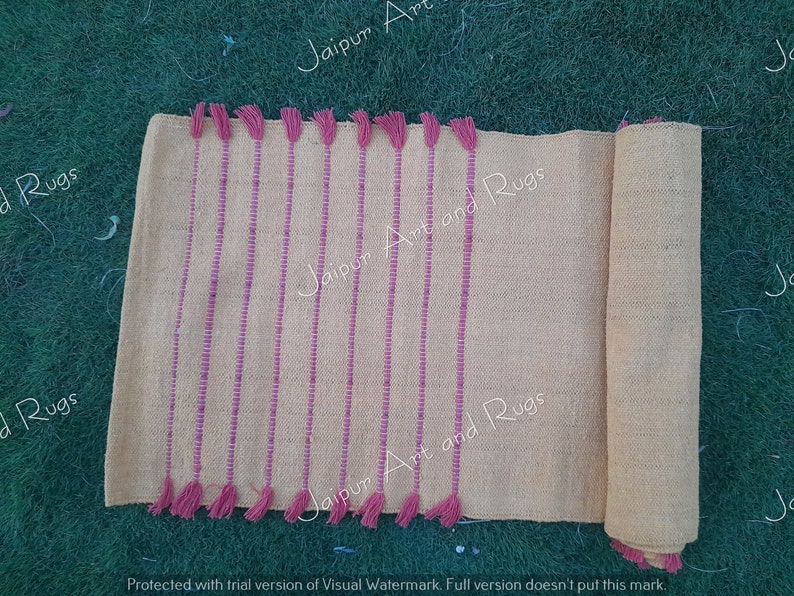 May include: A light beige runner rug with pink stripes and tassels. The rug is rolled up on the right side of the image. The text "Jaipur Art and Rugs" is visible on the rug.