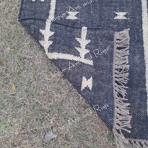 May include: A black and white patterned rug with fringe on the edges. The rug is made of woven cotton and has a geometric design.