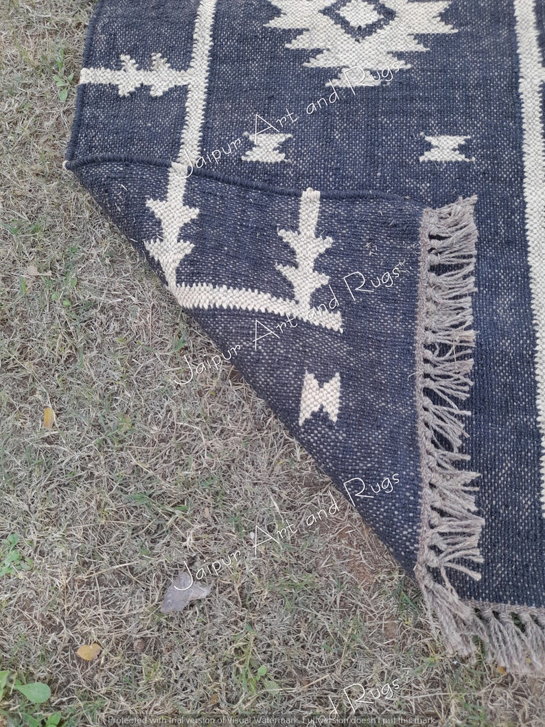 May include: A black and white patterned rug with fringe on the edges. The rug is made of woven cotton and has a geometric design.