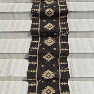 May include: Black and beige handwoven runner rug with a geometric pattern. The rug is laid out on a set of stairs. The text "Jaipur Art and Rugs" is visible on the rug.