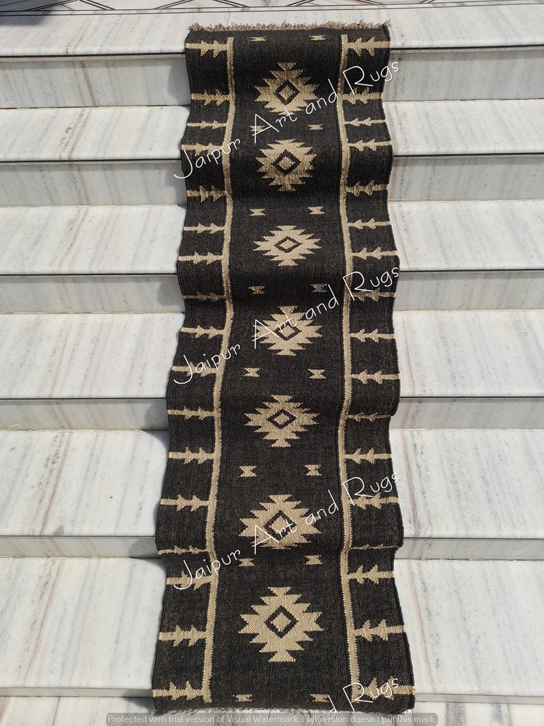 May include: Black and beige handwoven runner rug with a geometric pattern. The rug is laid out on a set of stairs. The text "Jaipur Art and Rugs" is visible on the rug.