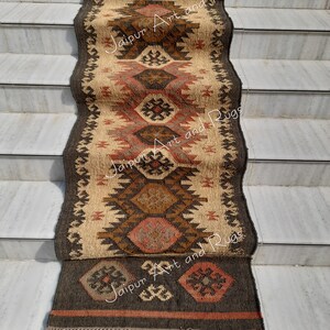 May include: A brown, beige and red patterned rug with fringe on the bottom. The rug is laid out on a set of stairs. The text "Jaipur Art and Rugs" is visible on the rug.