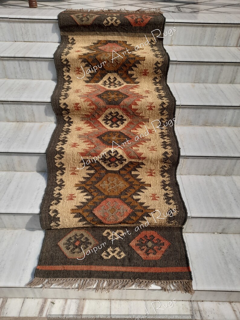 May include: A brown, beige and red patterned rug with fringe on the bottom. The rug is laid out on a set of stairs. The text "Jaipur Art and Rugs" is visible on the rug.