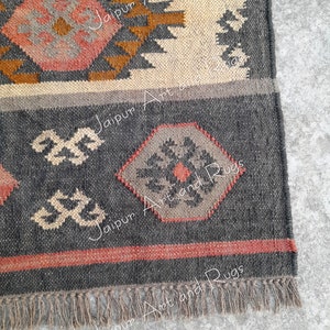 May include: Close-up of the bottom edge of a grey and brown woven rug with a geometric pattern. The rug has a fringe border and is made of natural fibres.