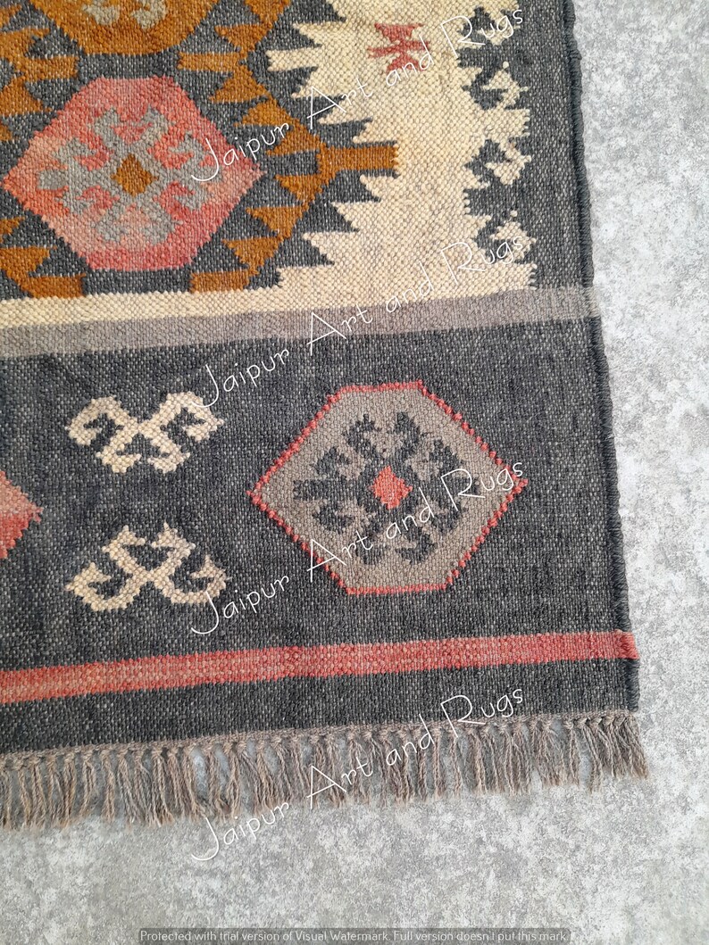 May include: Close-up of the bottom edge of a grey and brown woven rug with a geometric pattern. The rug has a fringe border and is made of natural fibres.